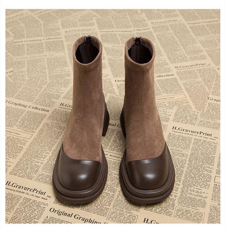 Pair of brown suede and leather ankle boots with front zipper on newspaper print background