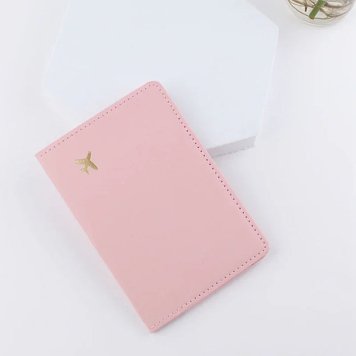 Pink leather passport holder with gold airplane embossed on white surface