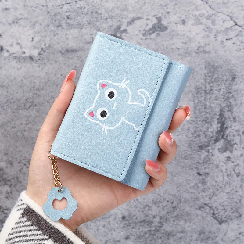 Hand holding a light blue wallet with cute cartoon cat print and flower keychain on gray background