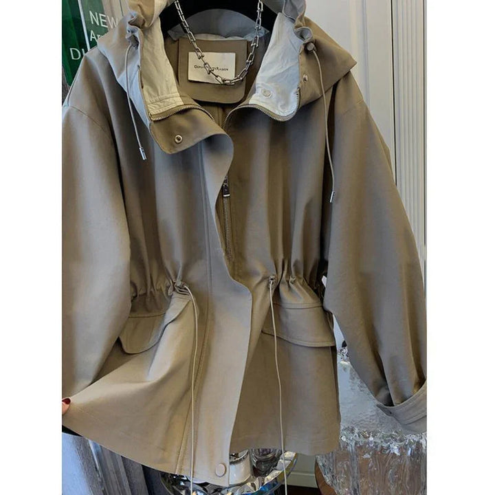 Beige hooded jacket with zipper and drawstring waist, displayed hanging indoors