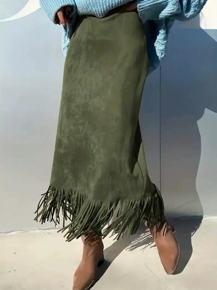 Woman wearing olive green suede fringe skirt and brown suede boots against white wall