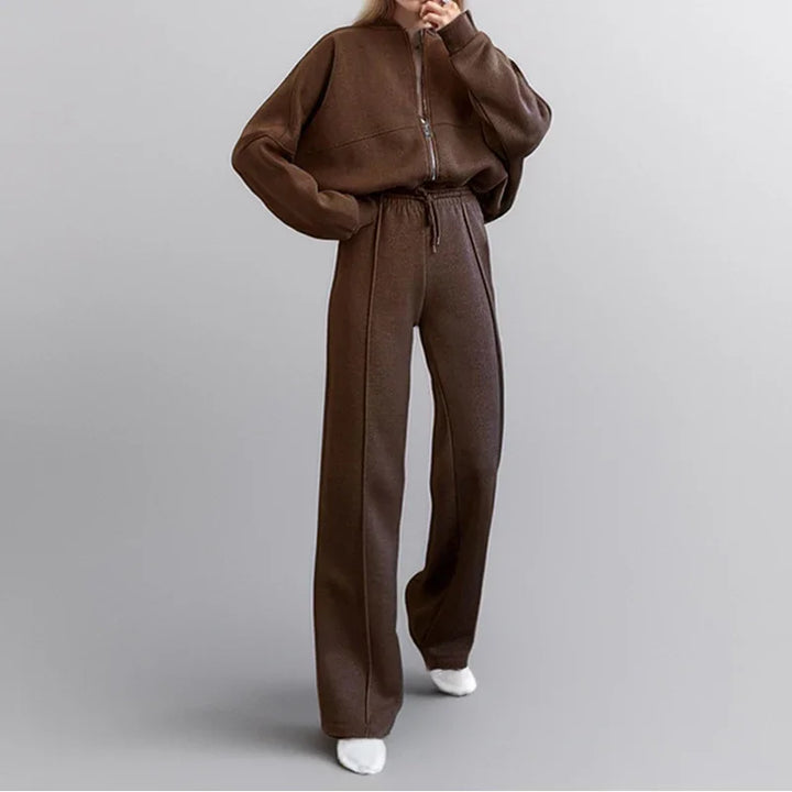 Woman wearing brown zip-up sweater and matching wide-leg pants with white shoes on gray background