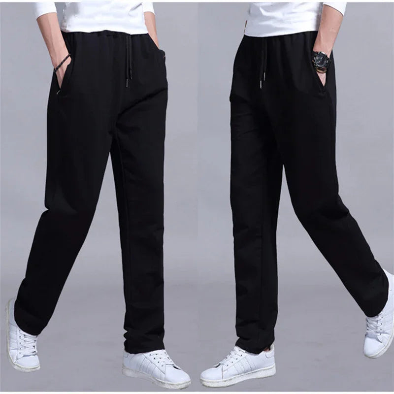 Men's black casual pants with elastic waistband and pockets, paired with white sneakers