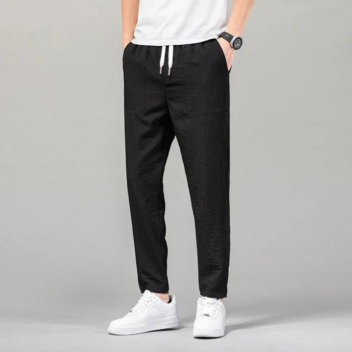 Man wearing black casual jogger pants with white drawstring and white sneakers on gray background