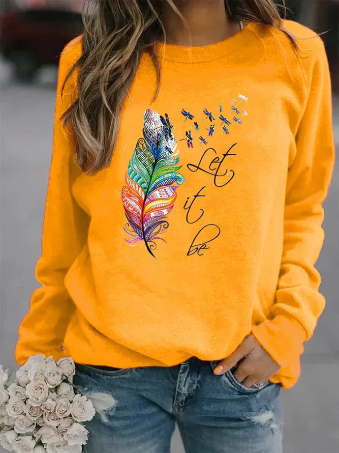 Woman wearing bright orange sweatshirt with colorful feather and dragonflies graphic and Let it be text