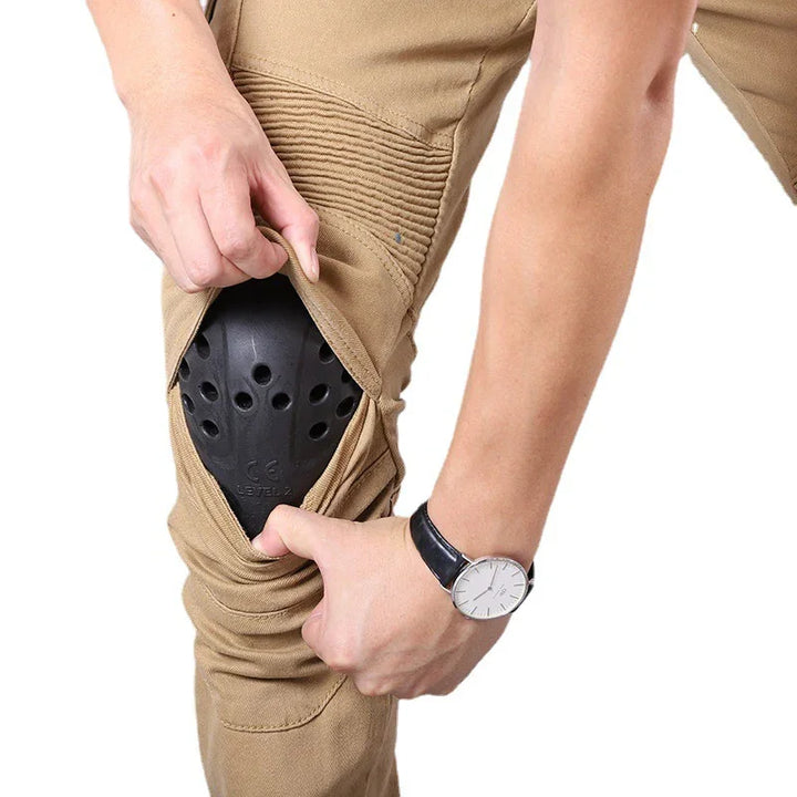 Close-up of person showing black protective knee pad inside tan motorbike pants