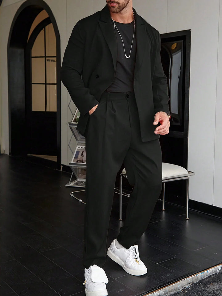 Man in black blazer and pants with black shirt and white sneakers in modern interior