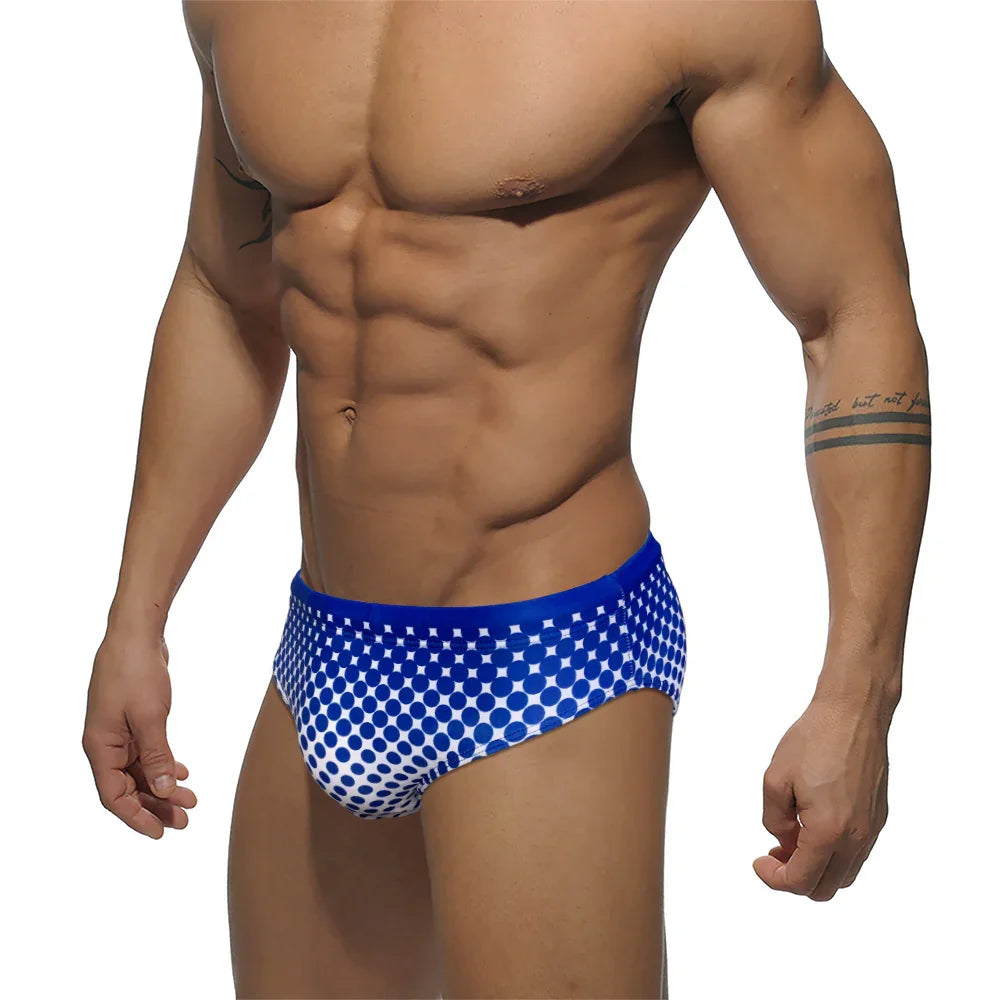 Muscular man wearing blue and white polka dot swim briefs against white background