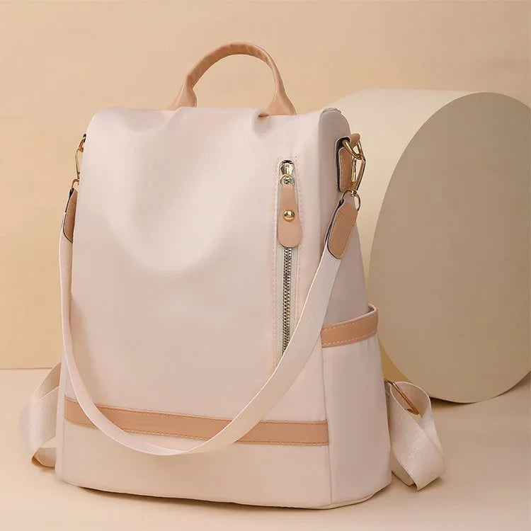 Beige minimalist backpack with tan leather accents and front zipper pocket on neutral background