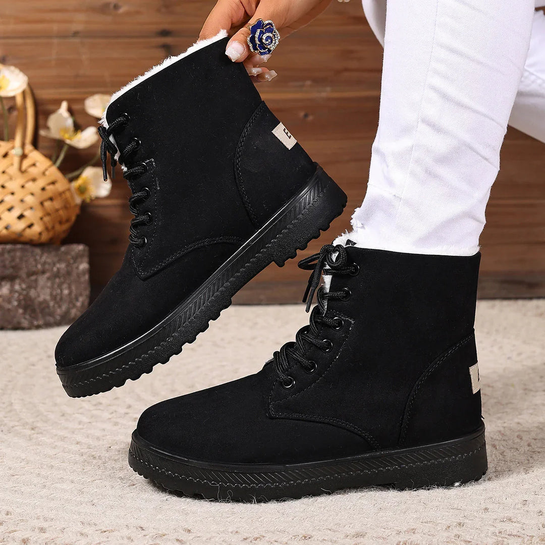 Black lace-up winter boots with white fleece lining worn with white pants on carpet