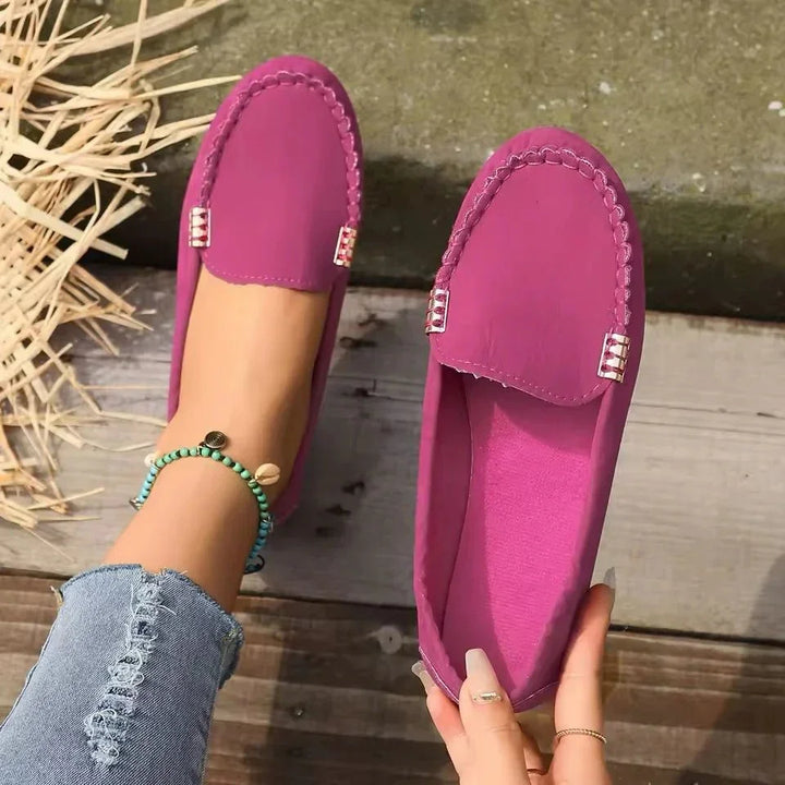 Woman wearing and holding purple moccasin loafers with distressed denim jeans and beaded anklet
