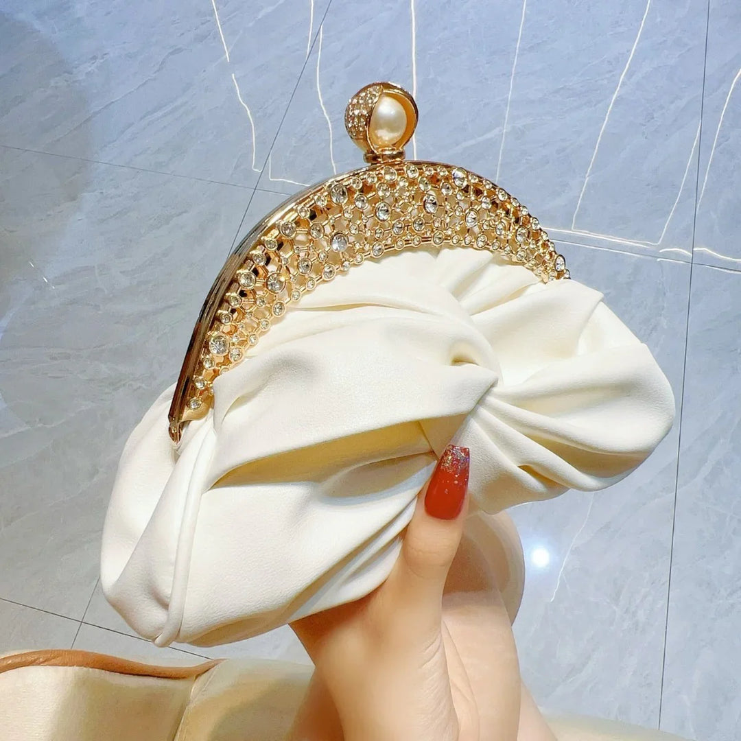 Hand holding ivory satin clutch purse with gold and rhinestone embellished frame and pearl clasp