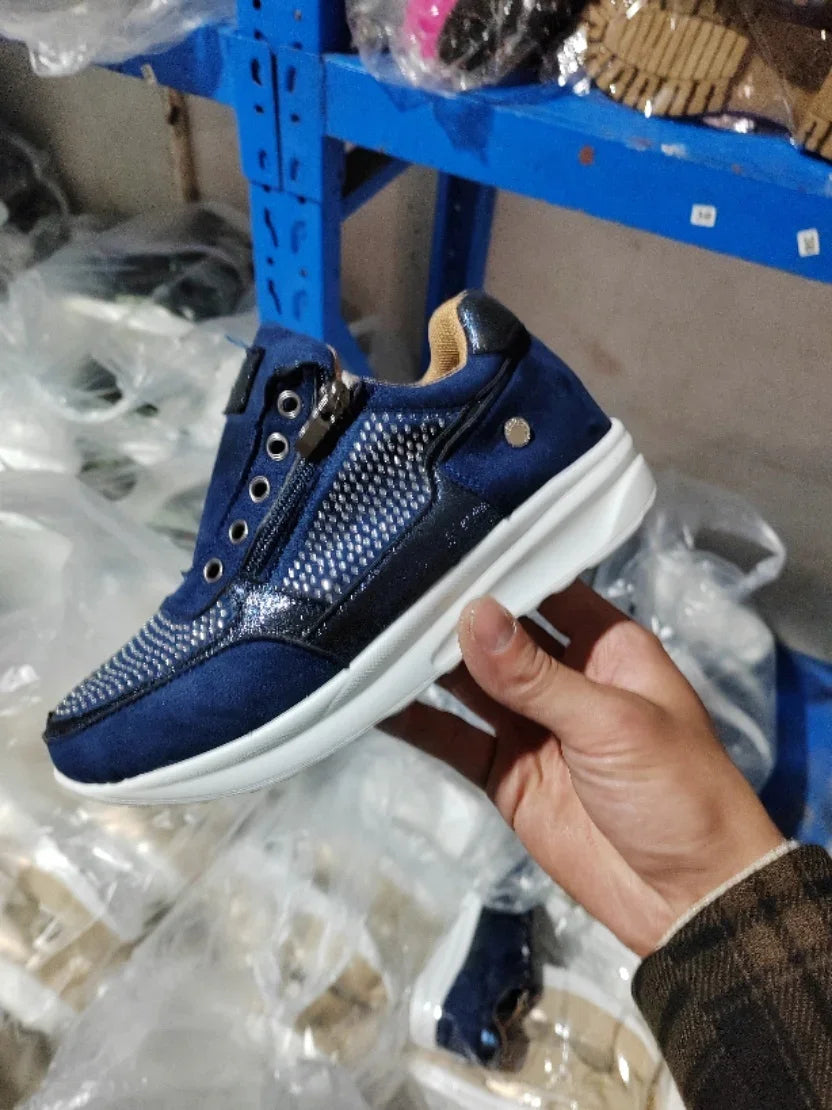 Hand holding blue sneaker with white sole, zipper detail, and breathable mesh upper in warehouse
