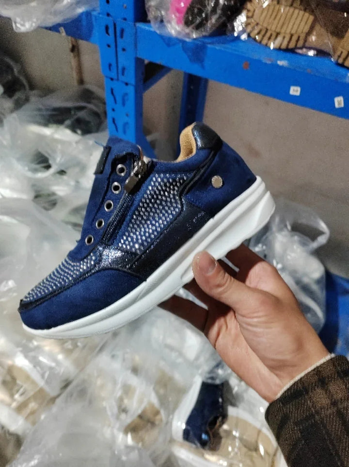 Hand holding blue sneaker with white sole, zipper detail, and breathable mesh upper in warehouse