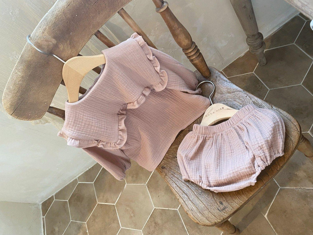 Pink ruffled baby outfit with long sleeve top and bloomers on wooden chair with hexagonal tile floor