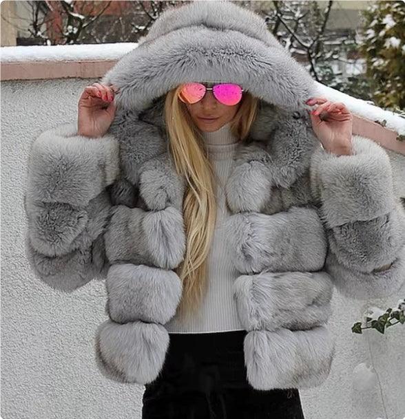 Woman wearing a luxurious gray fur coat with large hood and pink mirrored sunglasses outdoors in snowy setting