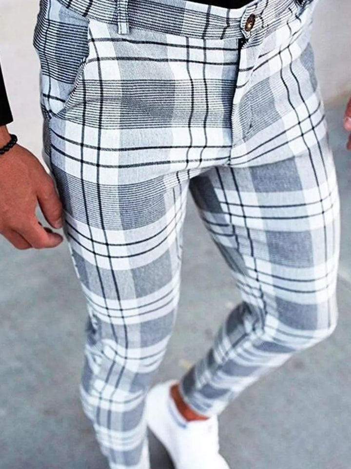 Close-up of men's slim fit gray and white plaid pants worn with white sneakers on concrete floor