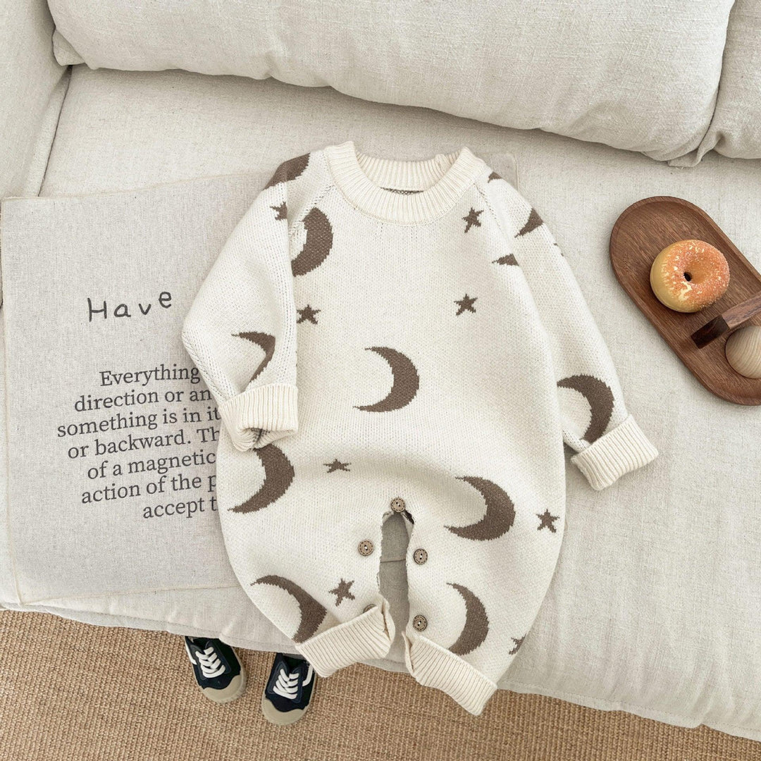 Cream baby onesie with brown moon and star patterns on beige cotton sofa