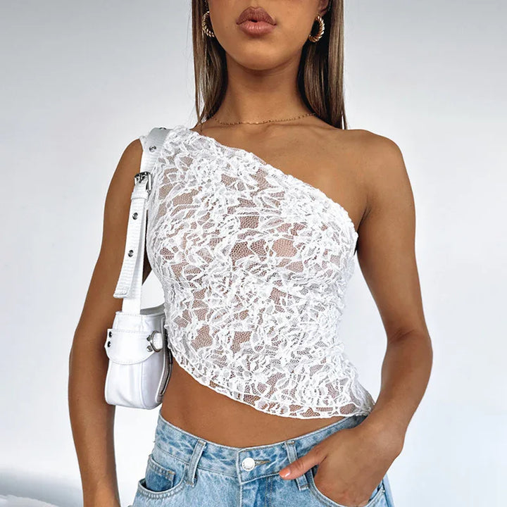 Woman wearing white one-shoulder lace crop top with blue jeans and white shoulder bag