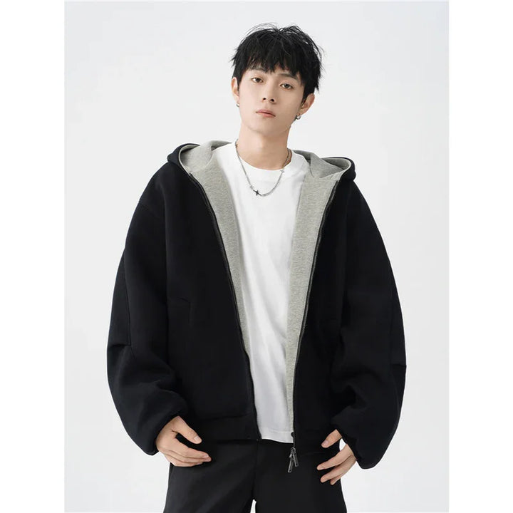 Young man wearing oversized black and gray hoodie with white t-shirt and black pants on white background