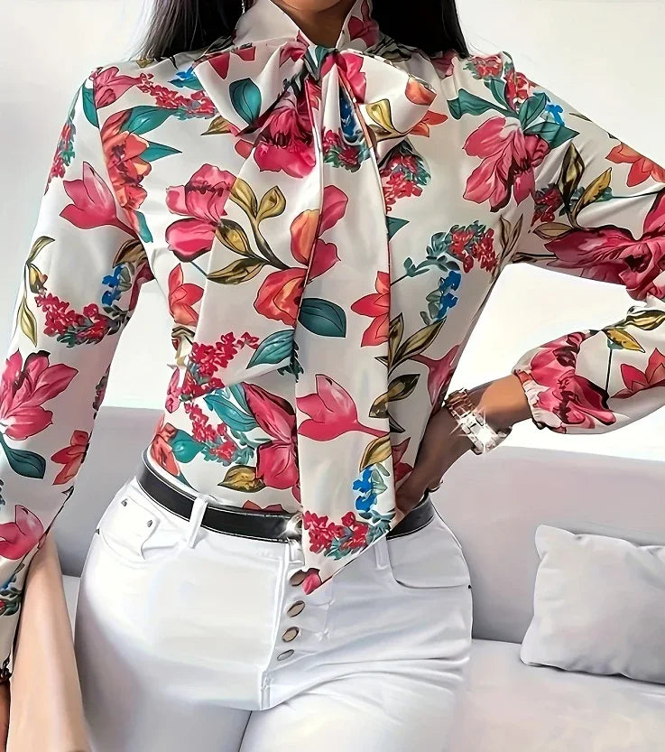 Woman wearing white floral blouse with pink, red, and blue flowers, paired with high-waisted white pants and black belt