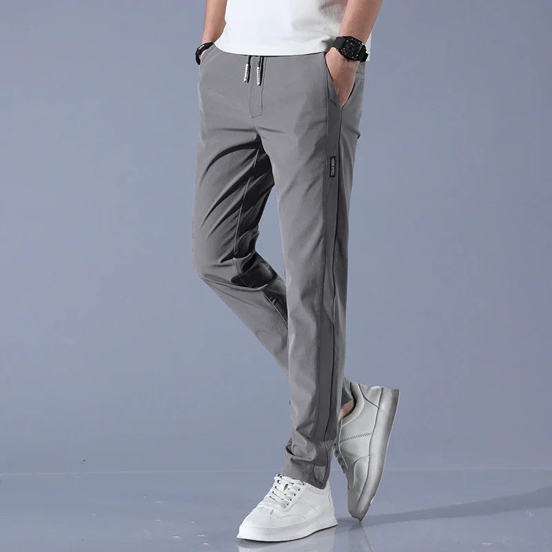 Man wearing slim fit gray casual pants and white sneakers on gray background