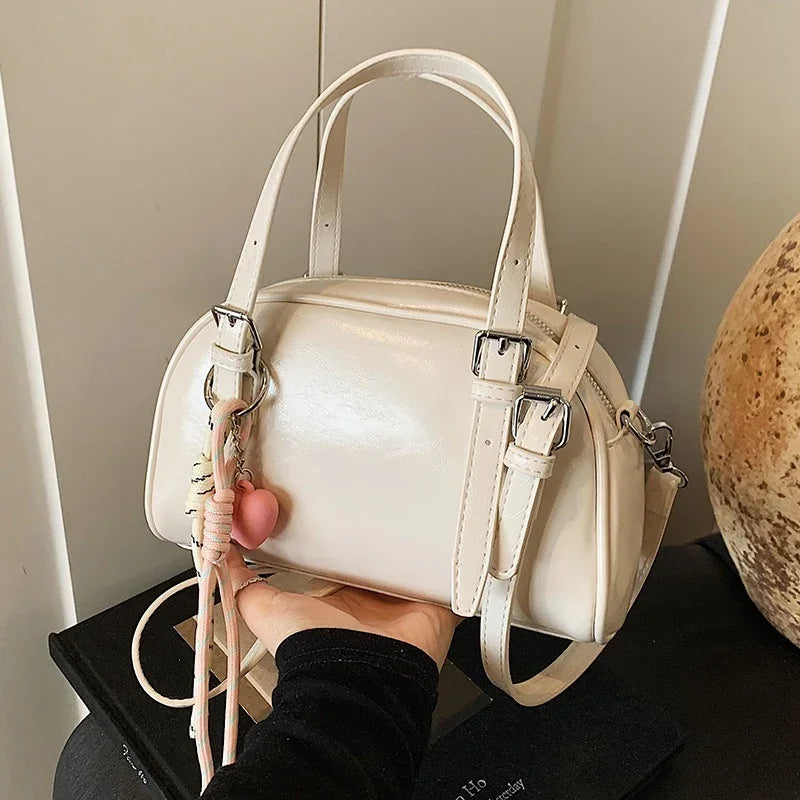 Small white leather handbag with double handles and decorative pink heart charm held over black books