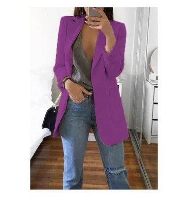 Woman wearing a purple blazer over a gray top with blue jeans, taking a mirror selfie indoors