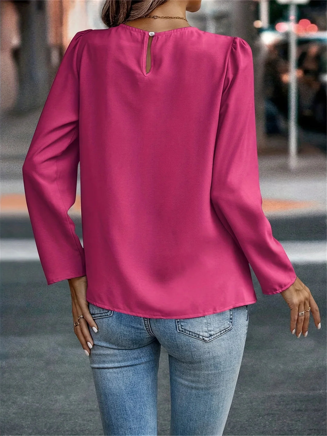 Woman wearing bright pink long-sleeve blouse with keyhole button back and light blue jeans