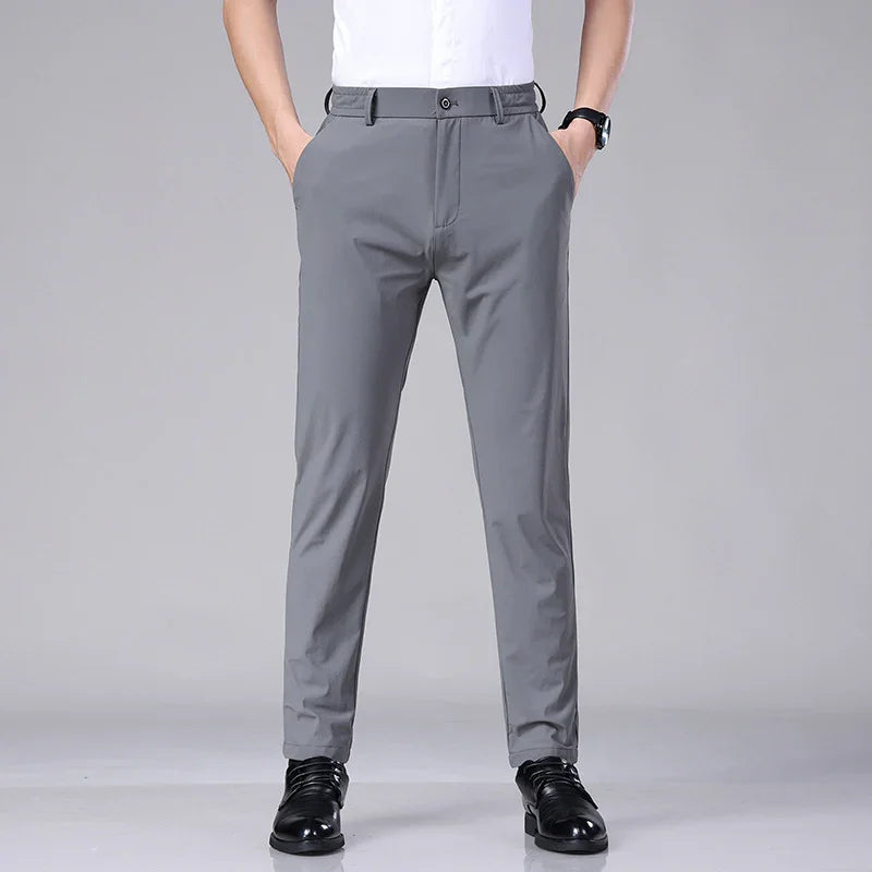 Man wearing gray slim-fit dress pants with black shoes and white shirt on gray background