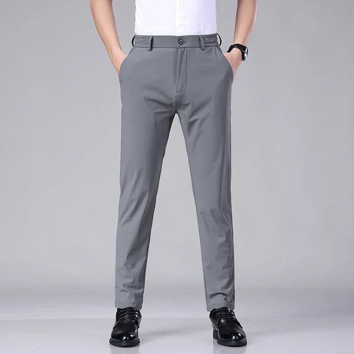 Man wearing gray slim-fit dress pants with black shoes and white shirt on gray background