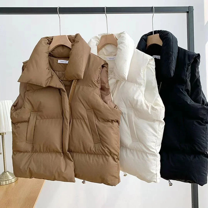 Brown, white, and black padded sleeveless puffer vests hanging on wooden hangers