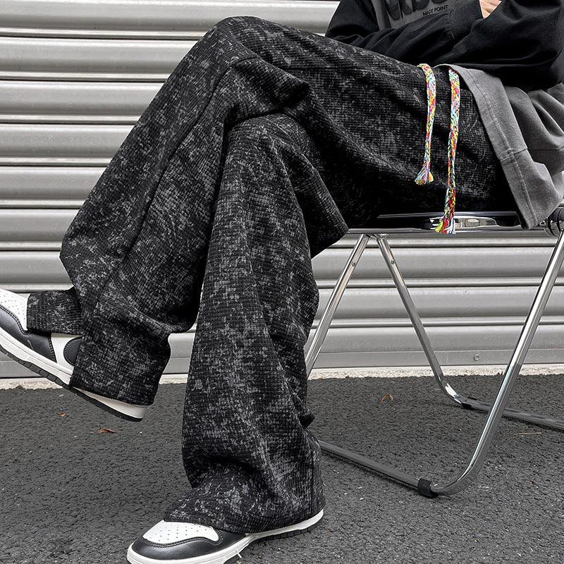 Person wearing black patterned wide-leg pants and black white sneakers sitting on a metal folding chair