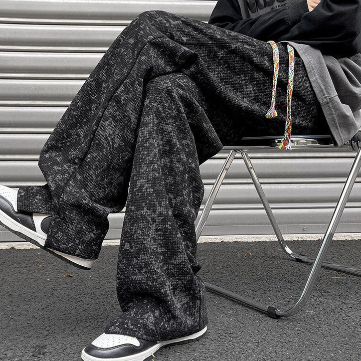 Person wearing black patterned wide-leg pants and black white sneakers sitting on a metal folding chair