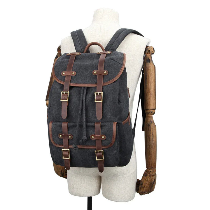 dark gray canvas backpack with brown leather straps and brass buckles on mannequin