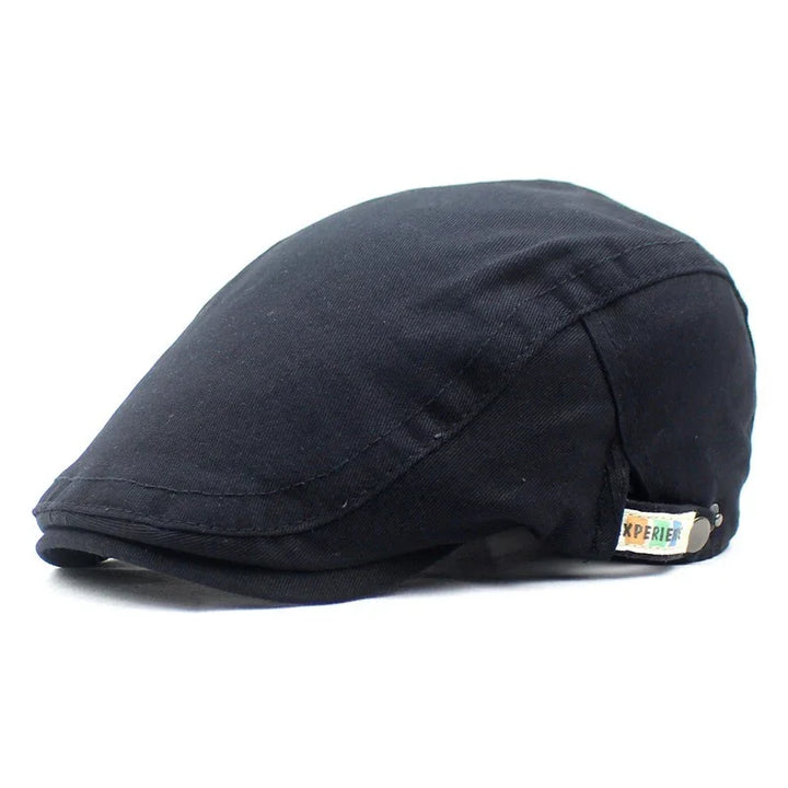 Black flat cap made of fabric with small sewn label on side against white background