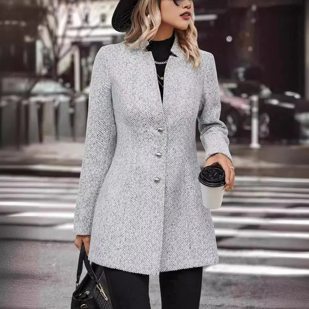 Woman wearing gray buttoned coat and black hat holding coffee cup and black handbag on city street