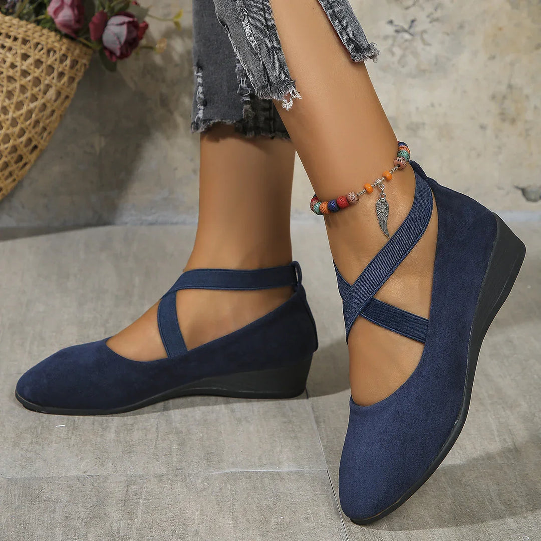Woman wearing navy blue wedge shoes with crossed straps and colorful beaded ankle bracelet