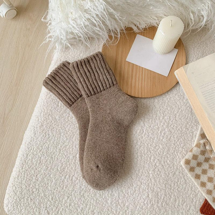 Cozy brown knit socks on a textured white blanket with a wooden tray, candle, and open book