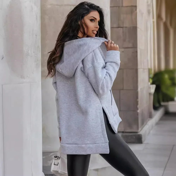 Woman wearing light gray hoodie and black leggings posing outdoors near stone pillars