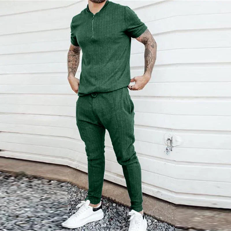 Man wearing green polo shirt and matching jogger pants with white sneakers against white wall