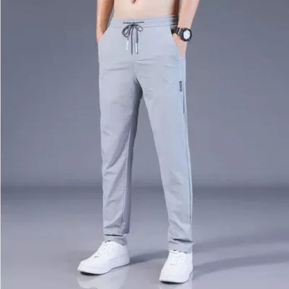 man wearing light gray casual pants with drawstring waist and white sneakers on gray background