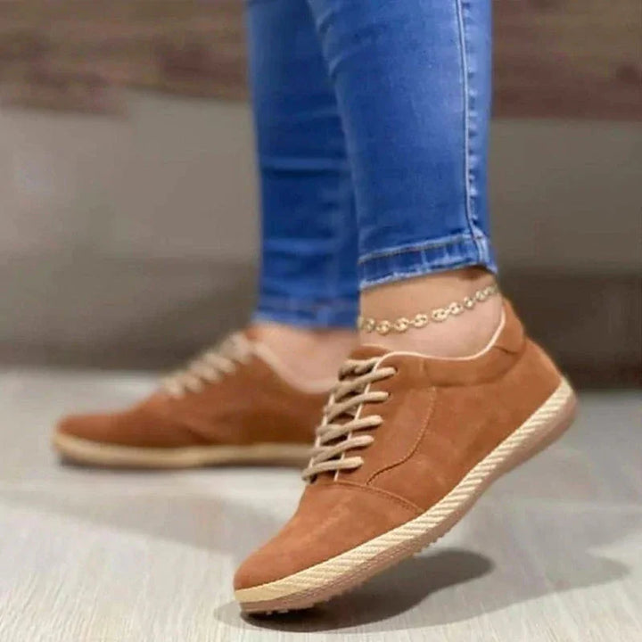 Close-up of brown suede casual sneakers with beige laces worn with blue skinny jeans and anklet
