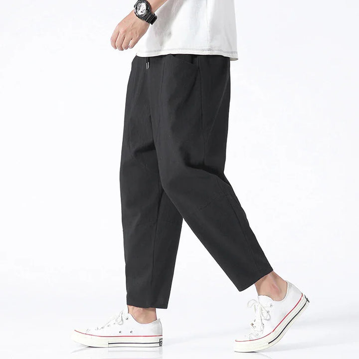 Person wearing black cropped pants and white sneakers with a visible wristwatch on white background