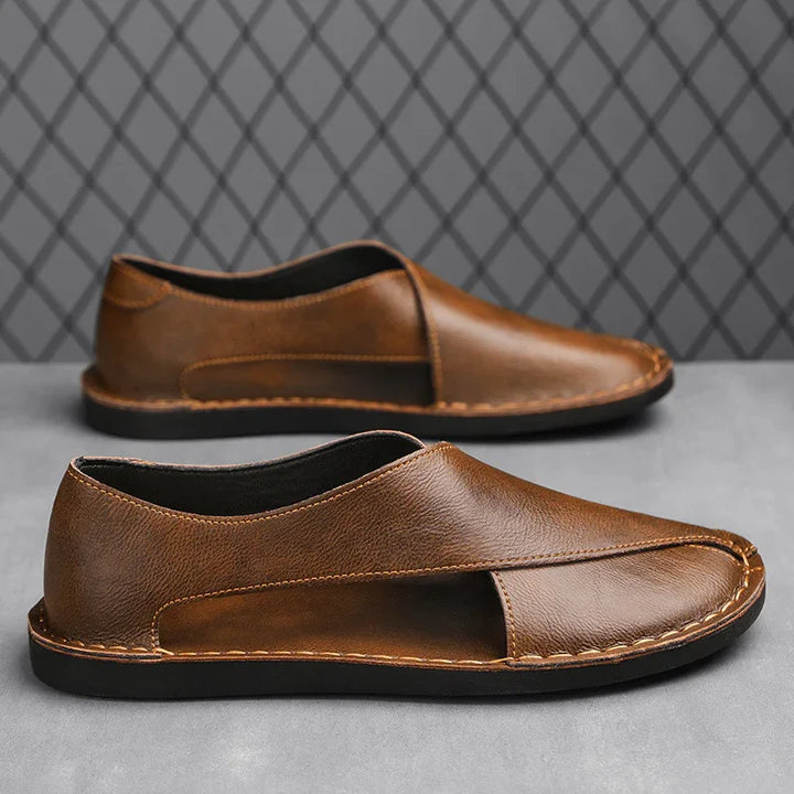 Brown leather slip-on shoes with black soles displayed on grey surface and diamond pattern background