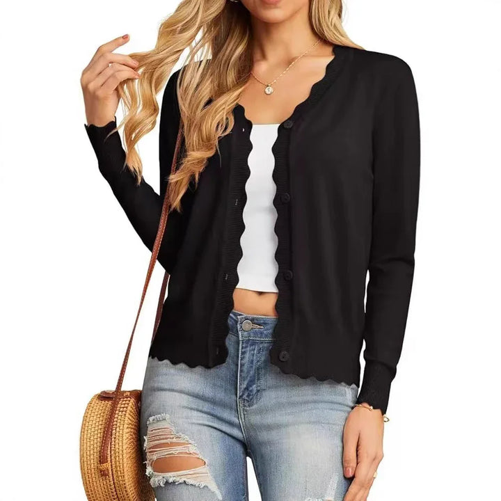 Woman wearing black button-up cardigan with scalloped edges, ripped jeans, white crop top, and round straw bag