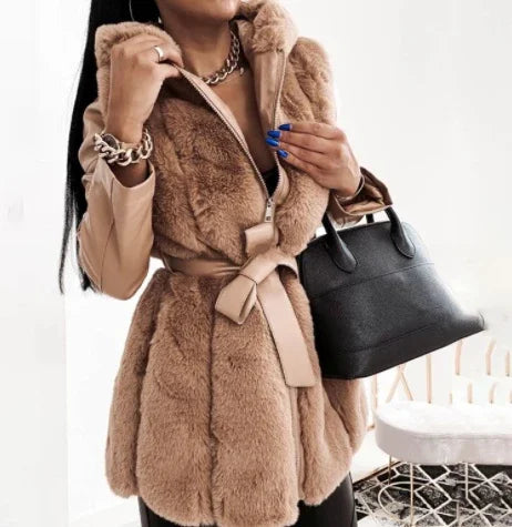 Woman wearing beige faux fur vest with belt, tan long sleeves, gold chain necklace and bracelet, holding black handbag
