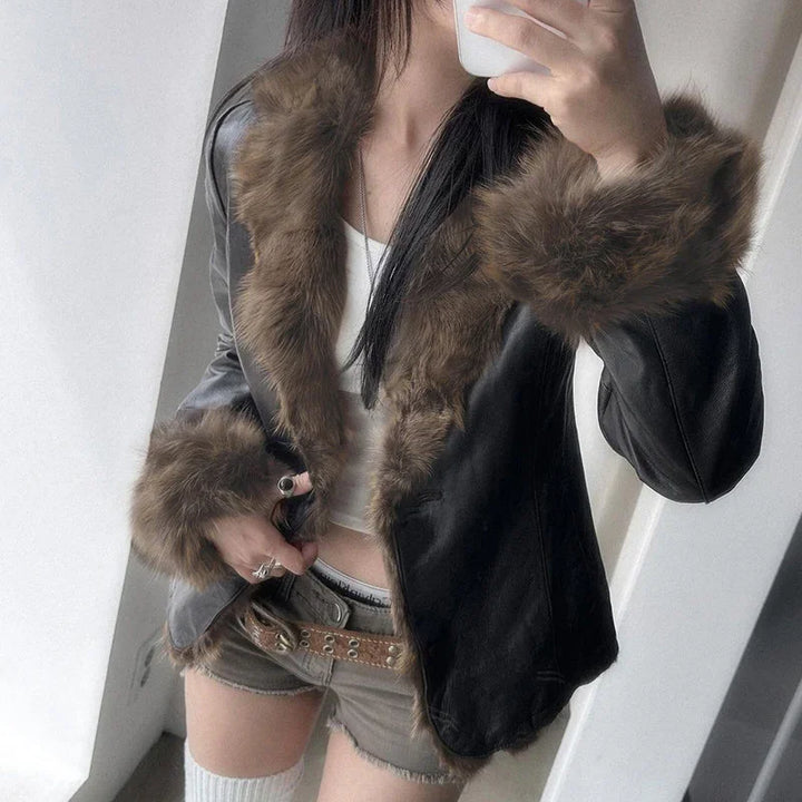 Woman wearing black leather jacket with brown fur trim and shorts taking a mirror selfie