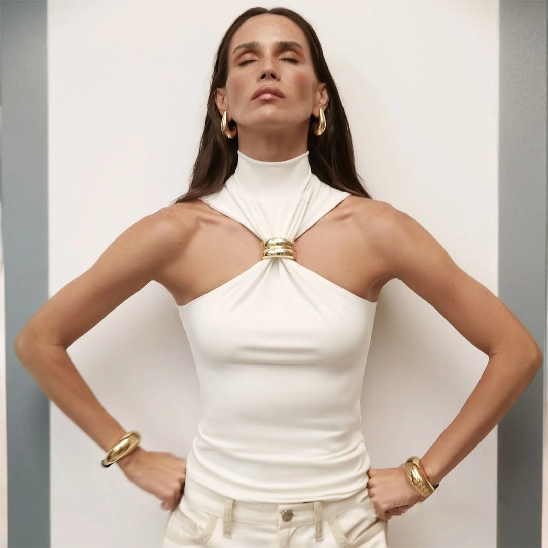 Woman in white halter top with gold ring detail and gold jewelry posing with eyes closed