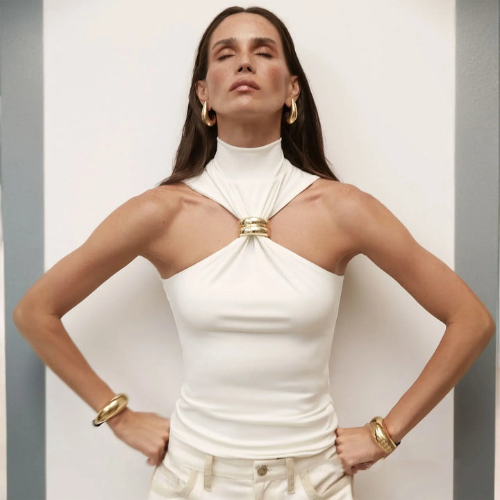 Woman in white halter top with gold ring detail and gold jewelry posing with eyes closed